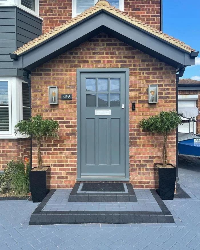 Grey composite front door with glazed panels on a brick porch